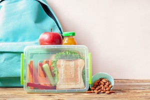 School lunch box with sandwich, vegetables, juice and almonds on table. Healthy eating habits concept.